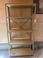 Front view of the beige metal shelving unit showing five shelves and cross-bracing on the back.