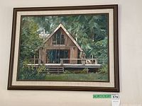Full view of the framed painting showing a wooden cabin surrounded by greenery and flowers.