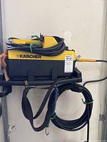 Side view of Karcher pressure washer on metal rack with hose coiled on top and yellow spray wand attached.