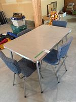 Full view of the retro table with leaf and four matching fabric-covered chairs with chrome legs in a basement setting.