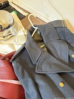 Gray military-style coat on a hanger, showing collar, epaulets, and buttons