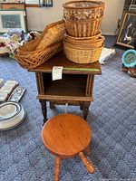 View showing small wooden side table, three-legged wooden stool with handle, and stacked wicker baskets on top of the table. Table shows a few scratches on the legs.