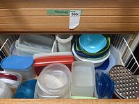Top view of a drawer filled with multiple plastic food storage containers with lids, bowls in blue, green, and white, and miscellaneous kitchen containers.