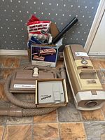 Full lot showing vintage Electrolux vacuum, power head, flexible hose, vacuum bags, and miscellaneous attachments grouped on floor.