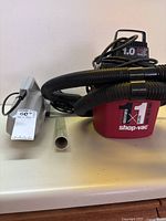 Shop-Vac 1 gallon wet/dry vacuum with attached black hose alongside a gray Hoover handheld vacuum brush.