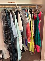 Full view of hanging women's clothing items on a rack showing variety of styles and colors including floral dresses, a teal velvet dress, plaid coats, and lightweight shirts