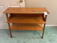 Wooden table with two shelves visible from the front, showing surface wear and natural wood finish.