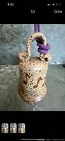 Front view of pottery bell with speckled finish and purple hanging cord.