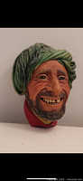 Close-up photo of a Bosson head wall hanging bust sculpture showing the man’s detailed facial features, green turban, and red garment with paint wear visible