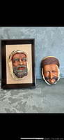 Photo showing two Bosson heads, one framed in a shadow box and one standalone, with detailed, naturalistic facial features and headscarves