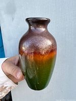 Photo of a hand holding a mid-century modern ceramic bud vase with a glossy gradient glaze shifting from green to orange and brown shades.