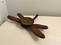 Single photo of a dark brown cast iron tealight candle holder shaped like a dragonfly, placed on a white surface.