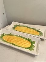 Two small rectangular ceramic plates with detailed raised corn decoration in yellow and green, set side by side showing front detail
