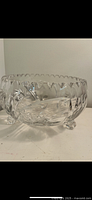 Clear crystal bowl with intricate cut and etched patterns, scalloped edges, standing on three feet.