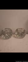 Photo showing two heavy clear crystal candle holders with detailed cut patterns from a side angle