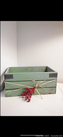Green wooden decorative box with metal corner protectors and tied faux red berries with raffia on front.