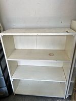 Full view of large handmade white wooden shelf showing three shelves and wax stains on top and middle shelf.
