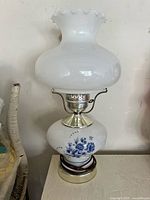 Full view of the milkglass lamp with ruffled glass shade, showing white and blue floral base and upper body.