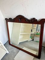 Mirror resting on the floor showing carved wood frame and chipping damage