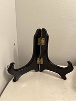 Photo showing the foldable black wooden plate stand set up and standing on a white surface against a light colored wall.