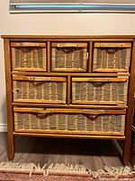 Front close-up of the wooden dresser showing the top row of three small woven wicker drawers with wooden frames and curved handles.