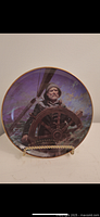 Front view of the decorative plate depicting an elderly sailor at the helm of a ship against a moody sea and sky background, with gold trim and a gold-tone stand.