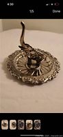 Silver elephant ring holder on decorative round dish base with floral edge.