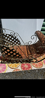 Photo showing a side profile of a vintage decorative sleigh with metal scroll designs and woven wicker seating area.