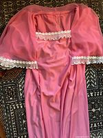 Photo showing pink vintage dress with flowing fabric, sheer overlay cape with lace trim along sleeves and bodice neckline