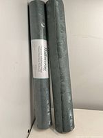 Two rolled wallpaper sheets in blue-green color with textured pattern, one sealed with label and one unsealed.