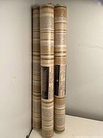 Three vertically standing wallpaper rolls, showing striped pattern in beige and tan shades.