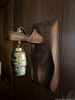 Close-up of wood wall lamp mounted on a wooden wall, showing the carved wood arm holding the metal bulb socket.