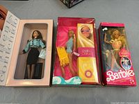 Photo showing all three Barbie dolls in their original boxes, side by side. Avon Barbie in light blue and black outfit, Malibu Barbie in bright yellow and blue box with towel, Ice Capades Barbie in pink box with skating outfit.