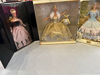 Three Barbie dolls in original boxes: Celebration Barbie in gold gown, Timeless Silhouette Barbie in pink and black gown, Peter Rabbit Barbie in themed box.
