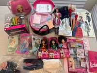 Photo showing multiple Barbie dolls with various outfits, Barbie accessory case, boxed dolls, and printed Barbie clothing packaging.