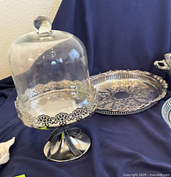 Silverplate cake stand with ornate pierced metal base and glass dome lid, black ribbon tied on pedestal