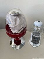 Photo of two candy dispensers side by side: the modern Brookstone Candy Man dispenser with a red base and transparent container, and a vintage-style white and glass gumball dispenser with coin mechanism.