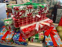 Seven decorative metal Christmas tins with various festive patterns and bows stacked together.