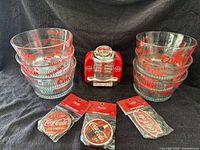 Lot arranged on black fabric background showing eight glass bowls stacked in two piles, one red miniature jukebox, and three unopened magnets in original packaging lined below.