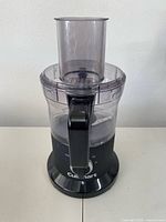 Front view of the Cuisinart food processor showing the clear plastic bowl and feed tube mounted on a black base.