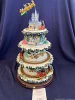Full view of the four-tier rotating Disney Christmas tree with holiday scenes, showing the castle on top and decorative base with snow effects.