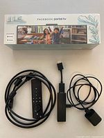 Facebook Portal TV sealed box with image of family on front, accompanied by Amazon Firestick, remote control, cables on white surface.
