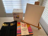 Full view of canvases, easel, paint brushes in case, and sealed acrylic paint box arrangement