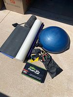 Wide shot showing all workout equipment including balance ball, foam rollers, resistance bands, mat, and push up tool