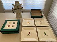 Porcelain angel figurine beside two sets of holiday plates, one set with four plates, the other missing one plate.