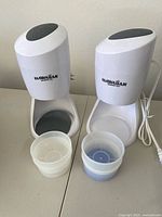 Two white Hawaiian Electric Shaved Ice Makers with four plastic bowls in front of them on a table.