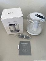 Photo showing Huaguo portable humidifier alongside its original box, USB cable, and user manual on a table.