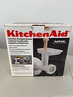 Front of the KitchenAid Food Grinder box, showing the product image and features including easy assembly, easy cleaning, and mass-free replacement warranty.