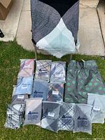 Thirteen shawl wraps, one spread open showing black, grey, light blue triangular design with fringed edge, others folded and individually bagged