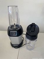 Nutri Ninja blender base with attached blending container and additional container with flip-top lid on table.